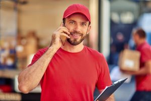 young cheerful caucasian male courier in red uniform talking on phone